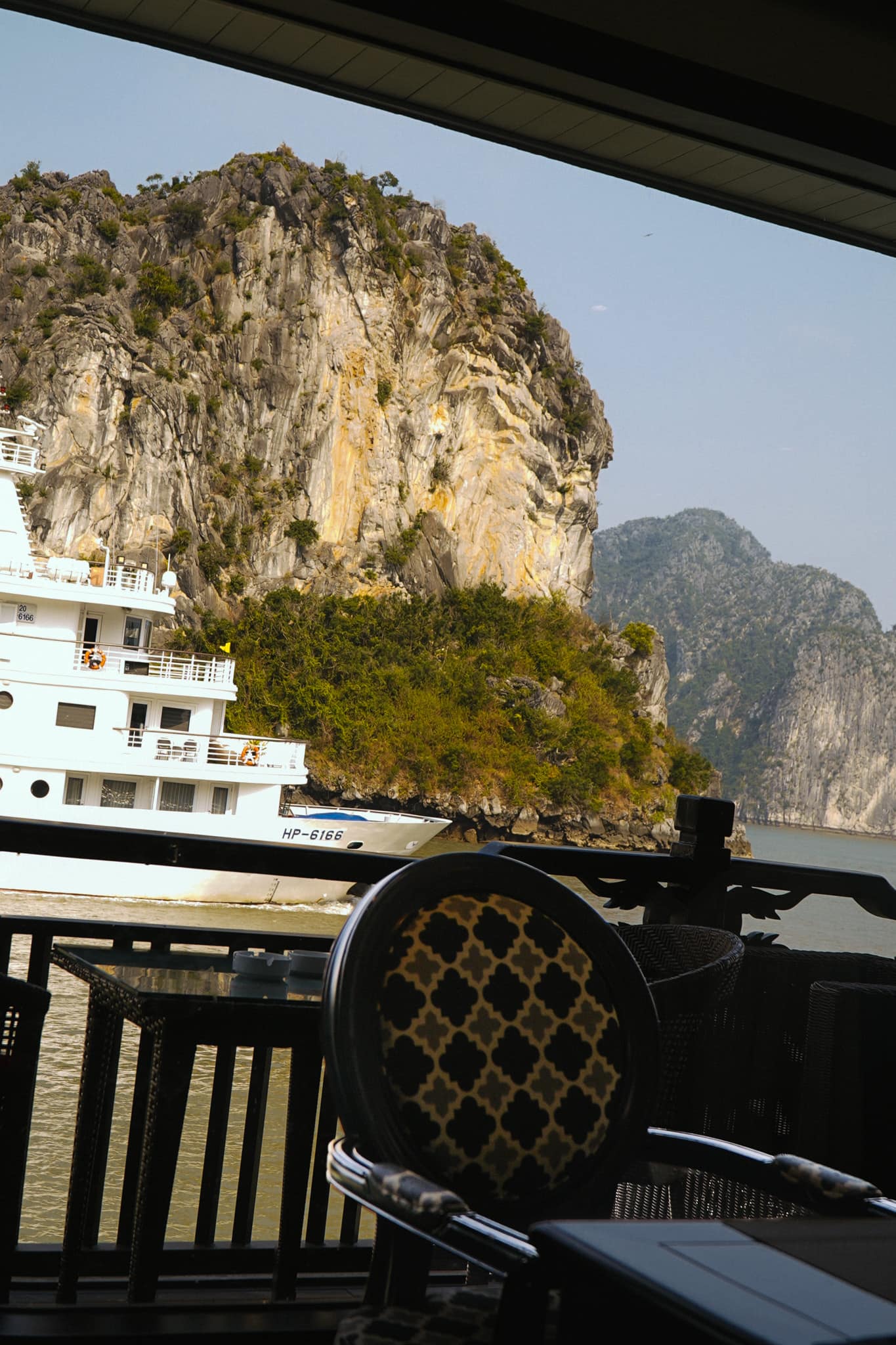A rattan chair on the deck, limestone cliffs and a moored boat beyond