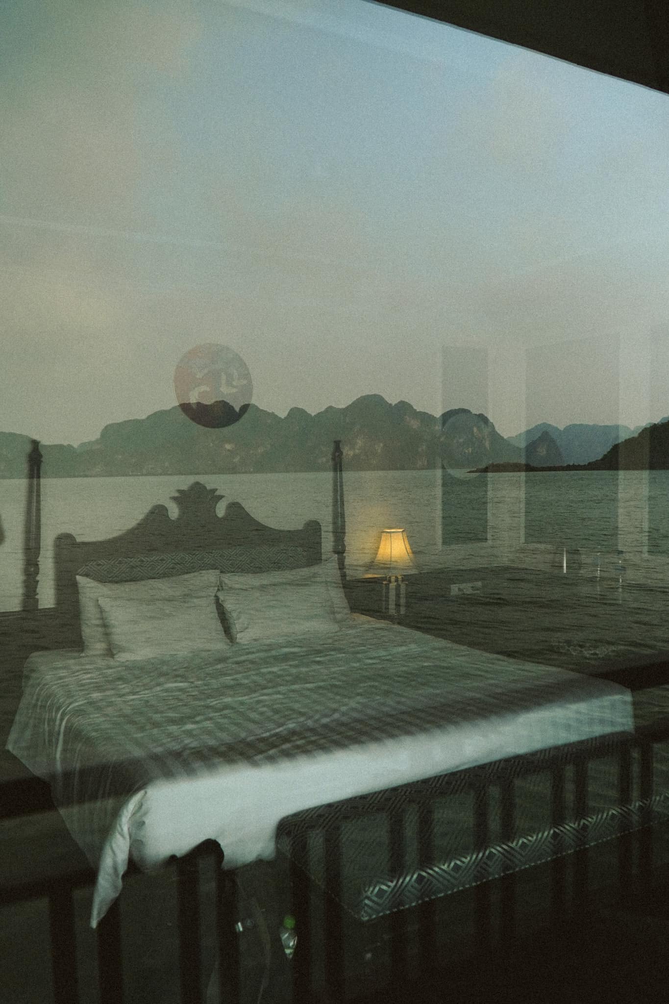 A bed beside a window, the bay and limestone islands reflected in the glass