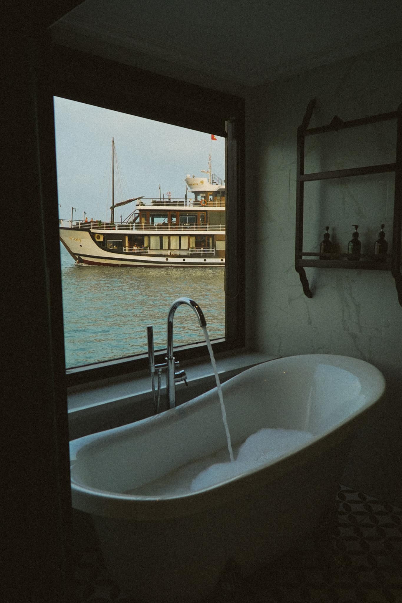A freestanding bath beside a window, a moored boat and limestone cliffs outside