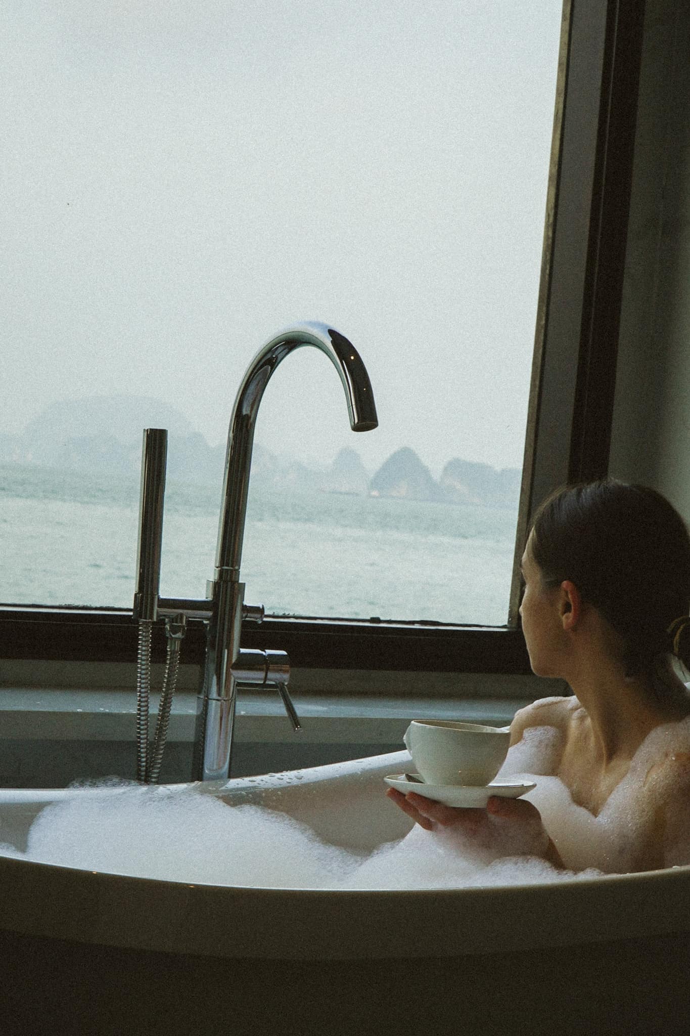 Holding a coffee cup in the bath, the bay through the window