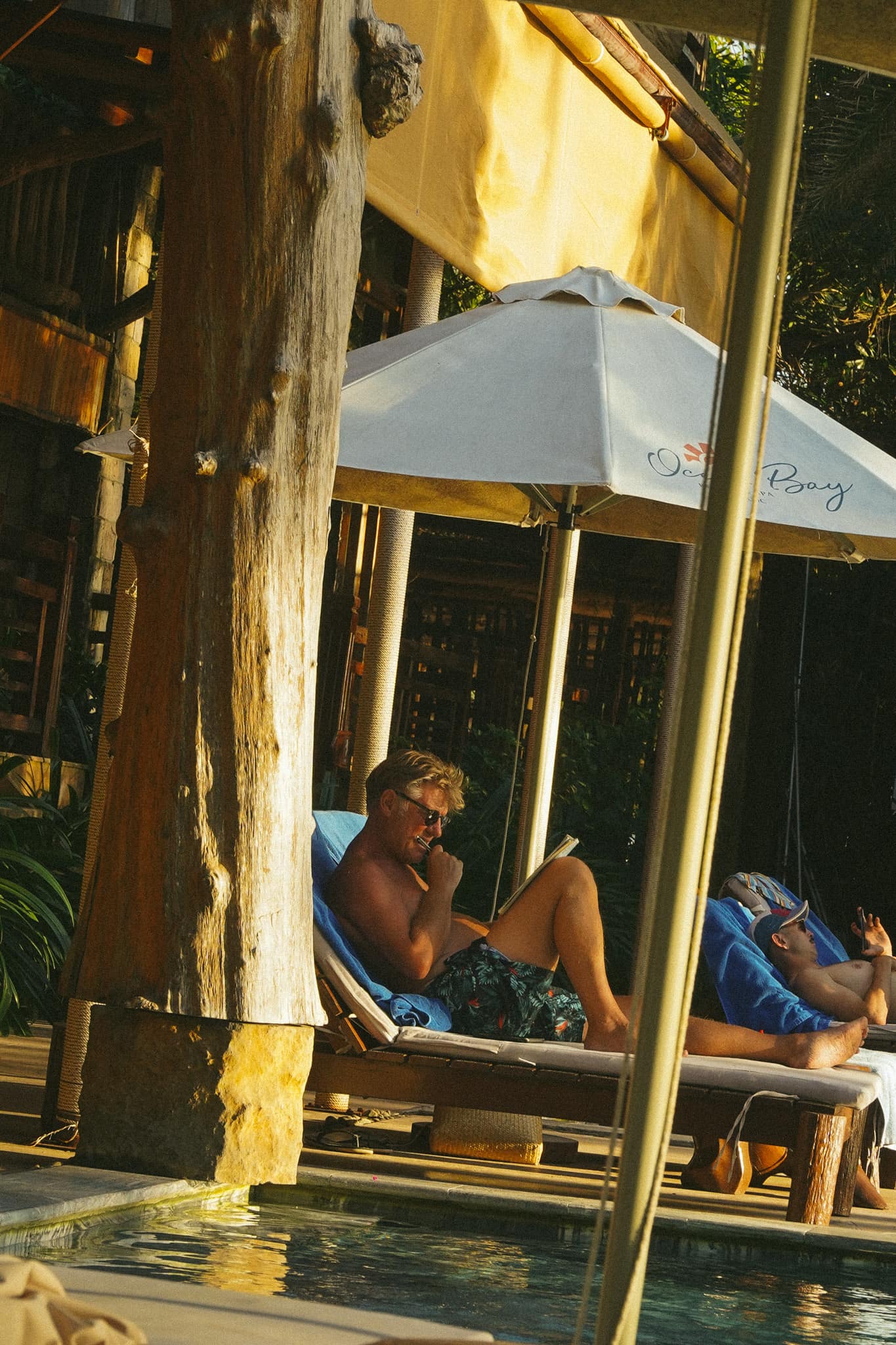 Reclining on a sun lounger beside the pool under a white umbrella