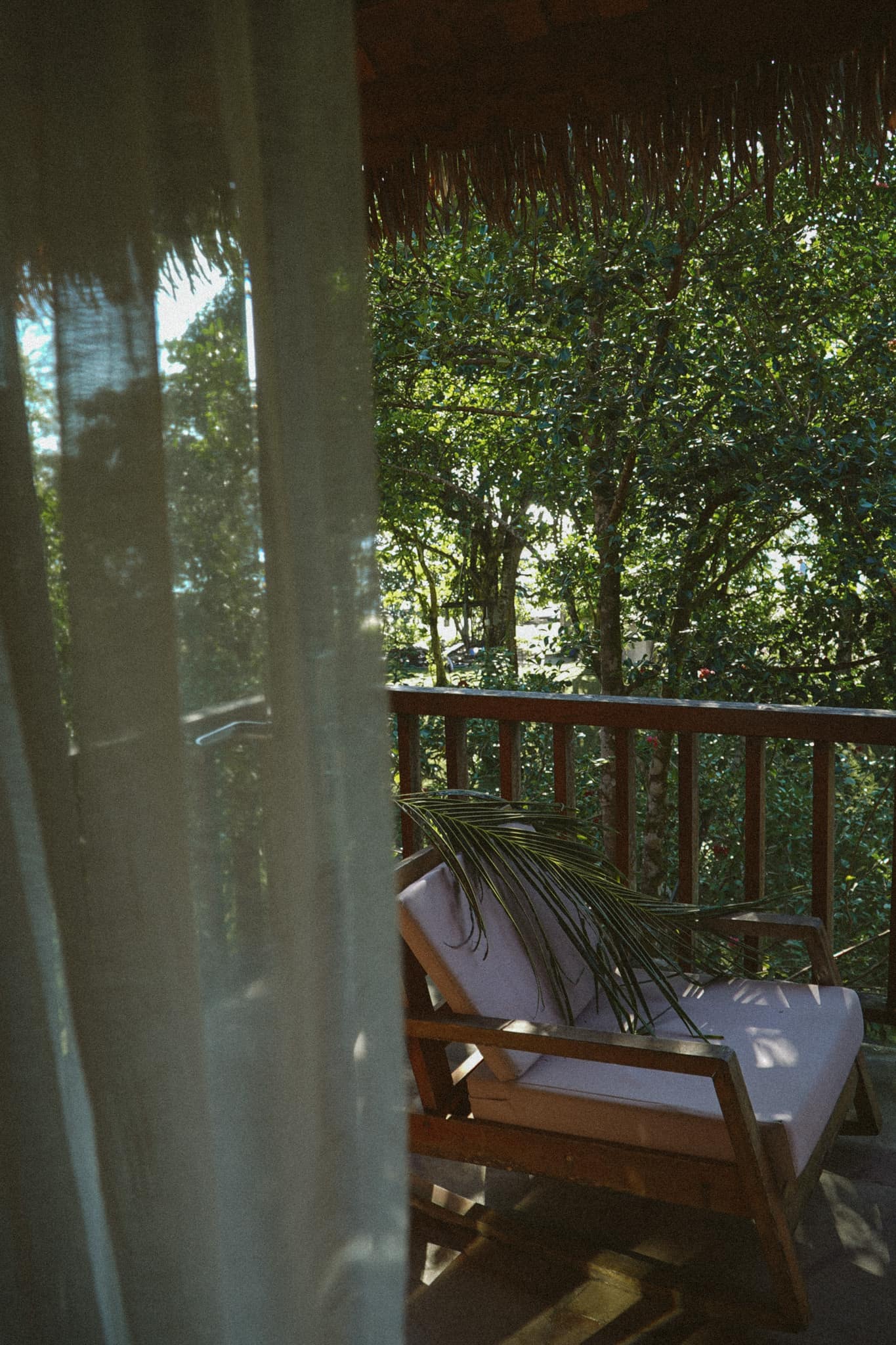 A sheer curtain drawn back from a balcony, chairs facing the trees