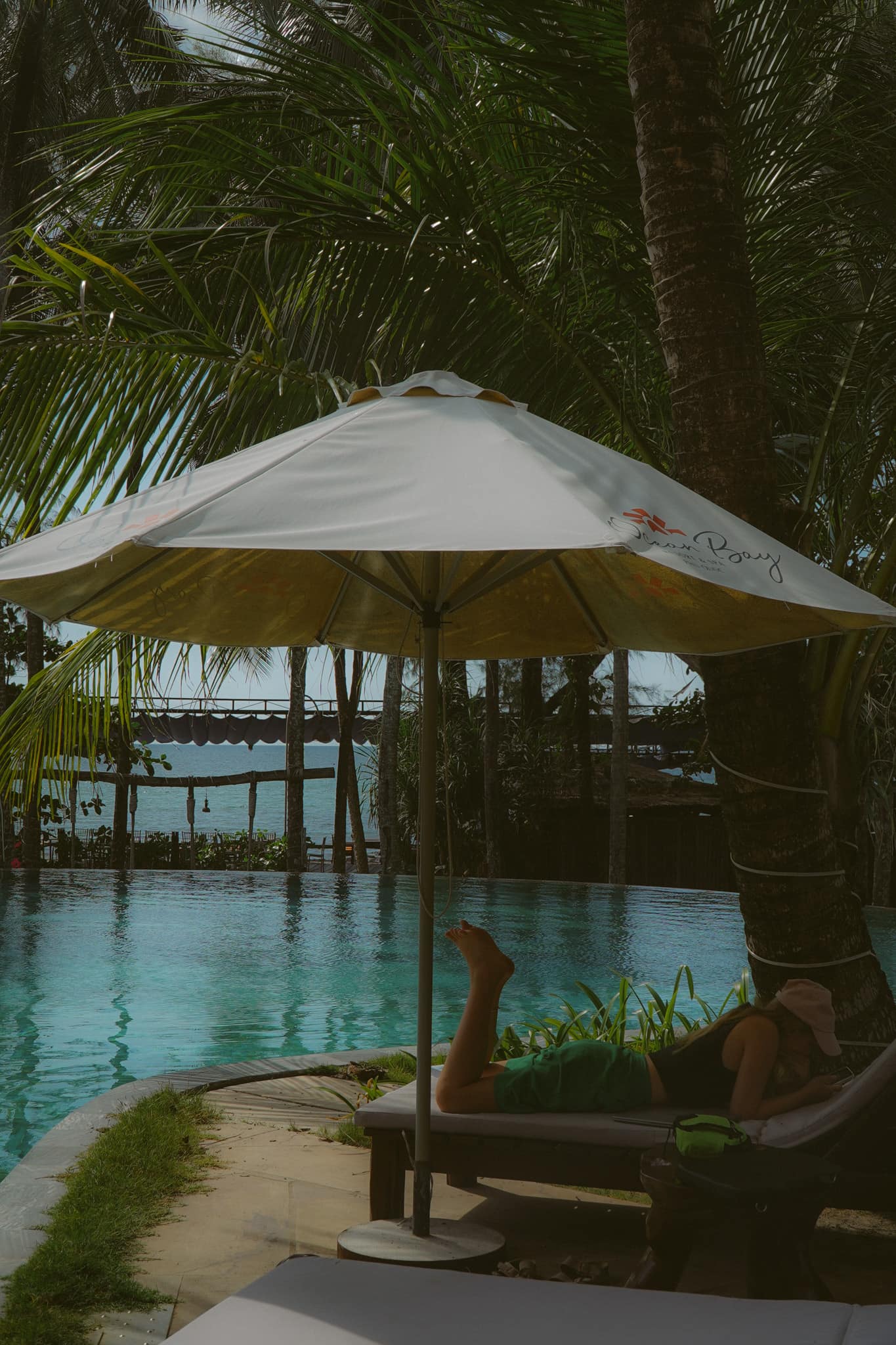A canvas umbrella over the pool, the sea and a jetty beyond