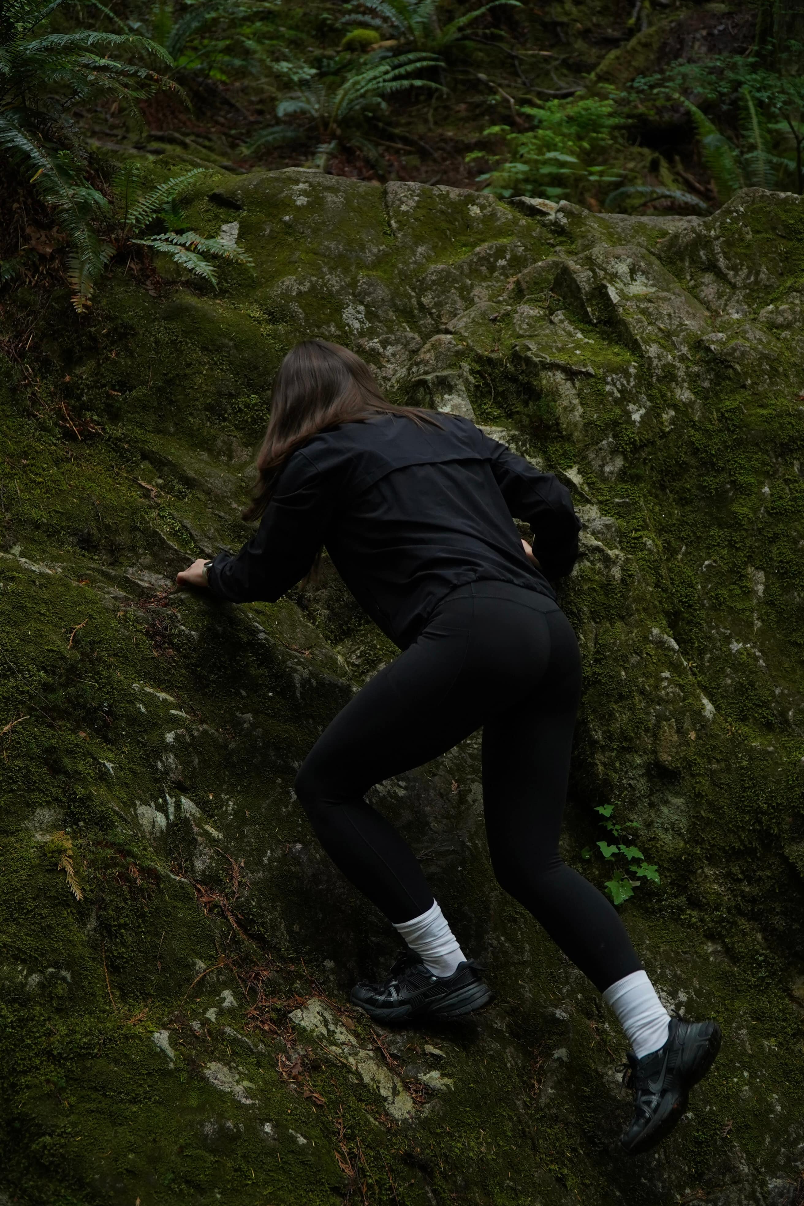 Scrambling up a moss-covered rock face in an Athleta jacket and leggings