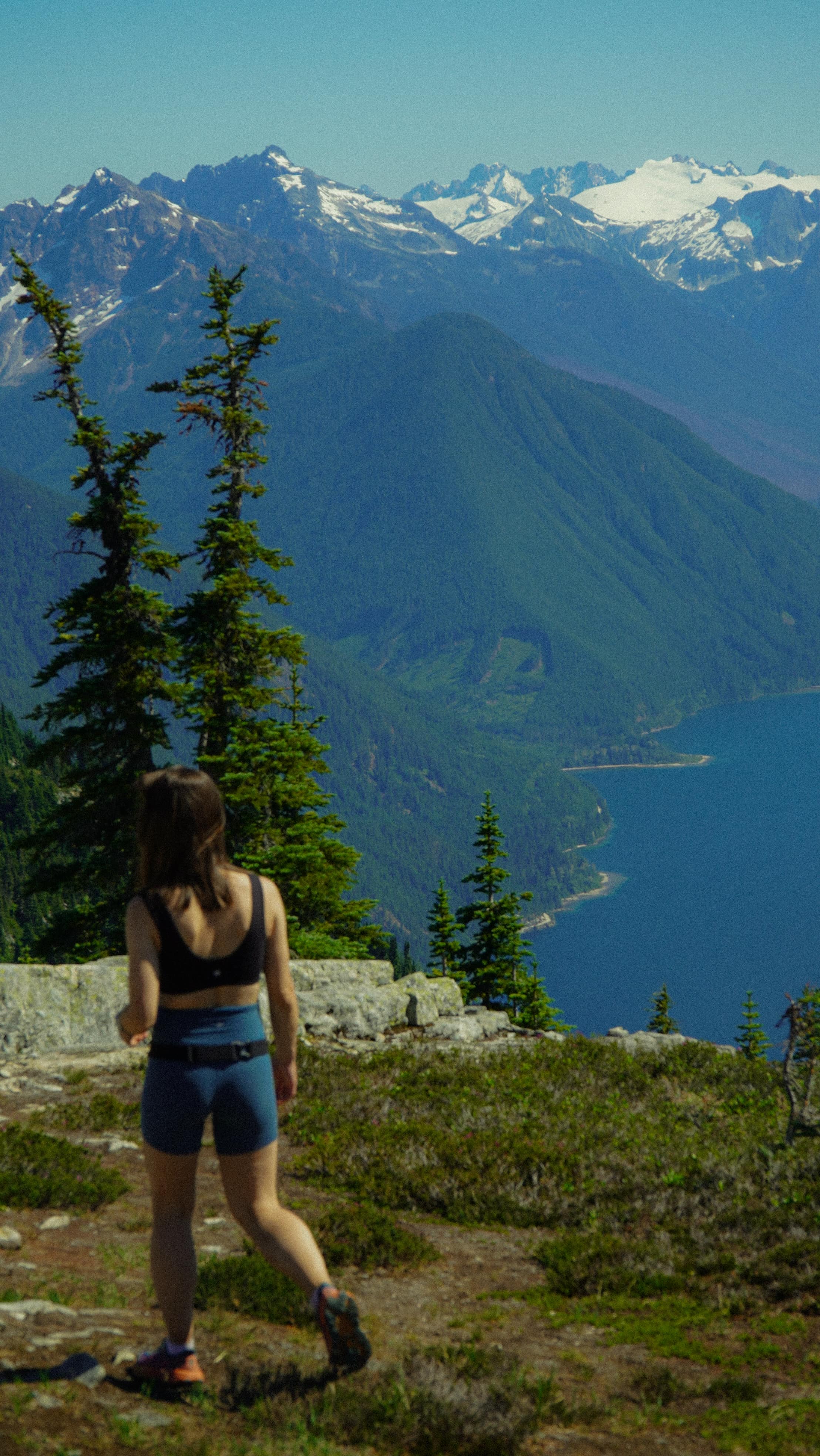 Walking toward the edge of an alpine meadow, a blue lake and glaciated peaks below
