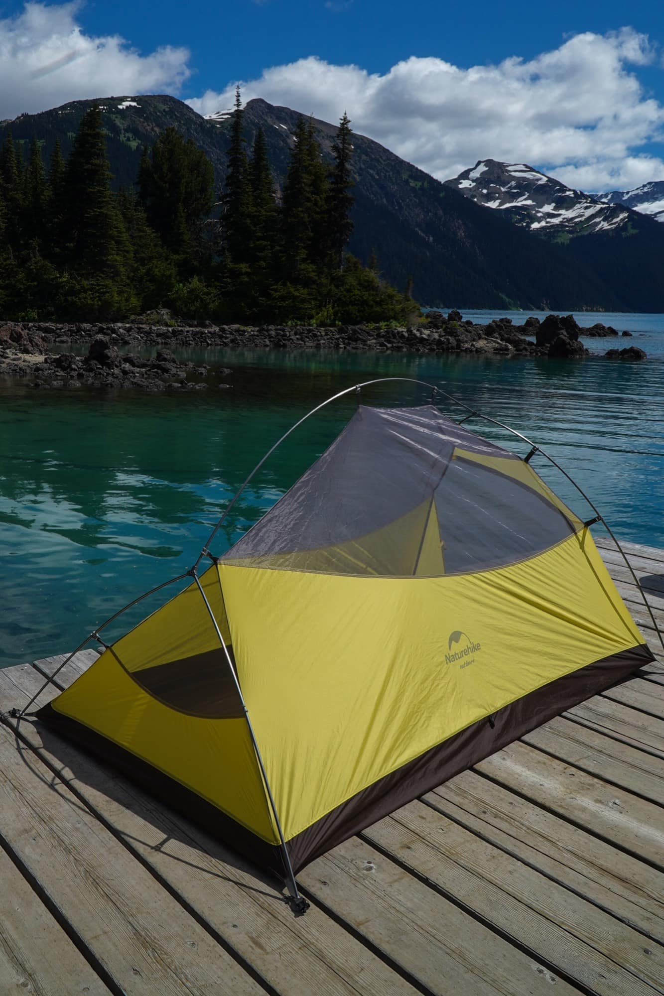 A Naturehike tent pitched on a dock above a turquoise lake